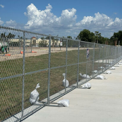 Temporary chain-link fencing installed along a sidewalk at a construction site in Southwest Florida, secured with sandbags for stability.