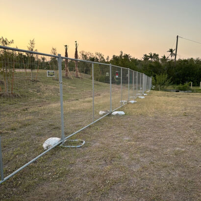 Freestanding temporary fence panels used for event or property security at sunset, supported by sandbags on a grassy lot.